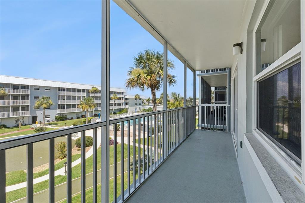A screened-in balcony overlooks a grassy courtyard with palm trees and a swimming pool — 315 N CAUSEWAY UNIT B302, NEW SMYRNA BEACH, FL