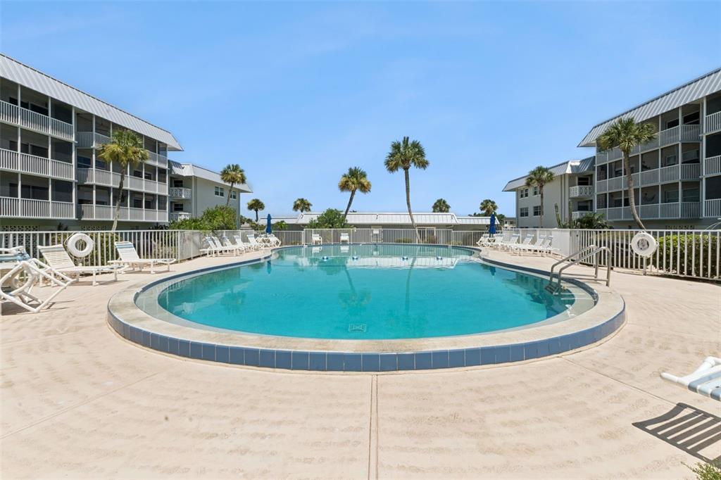 A swimming pool sits between two multi-story apartment buildings with palm trees and lounge chairs — 315 N CAUSEWAY UNIT B302, NEW SMYRNA BEACH, FL