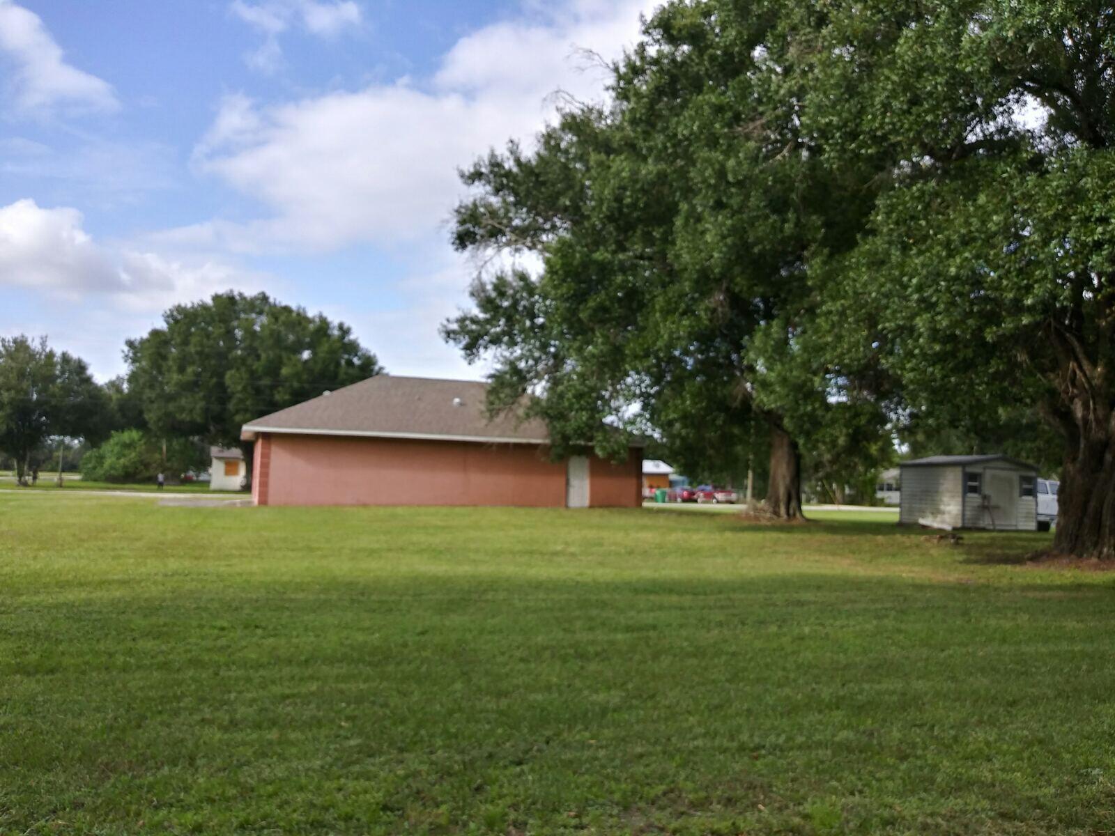 A large grassy yard features a pink building, a small shed, and mature oak trees — 810 NW 10th Street, Okeechobee FL 34972, OKEECHOBEE, FL