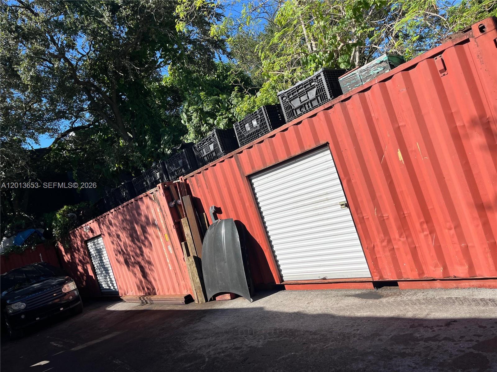 Two red shipping containers with roll-up doors sit outdoors next to a parked black vehicle — 1780 NW 21st Ter, Miami FL 33142, MIAMI, FL