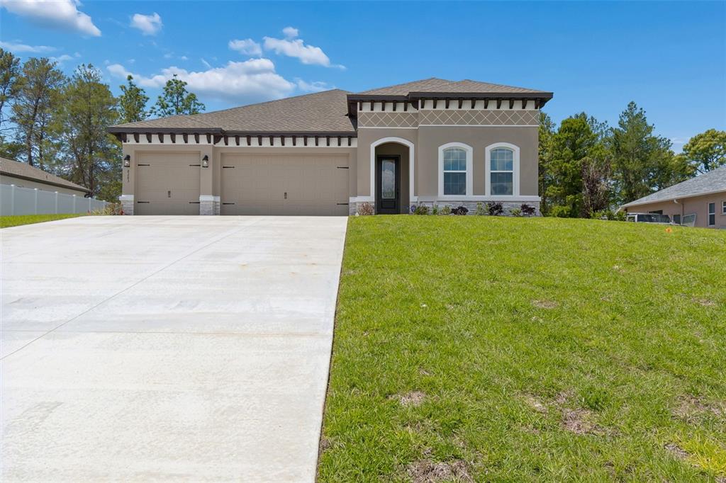 A single-story house with a tan stucco exterior, a three-car garage, and a concrete driveway — 8283 NITTANY ROAD, WEEKI WACHEE, FL