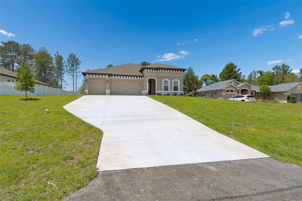 A single-story house with a concrete driveway, two-car garage, and a tan stucco exterior — 8283 NITTANY ROAD, WEEKI WACHEE, FL