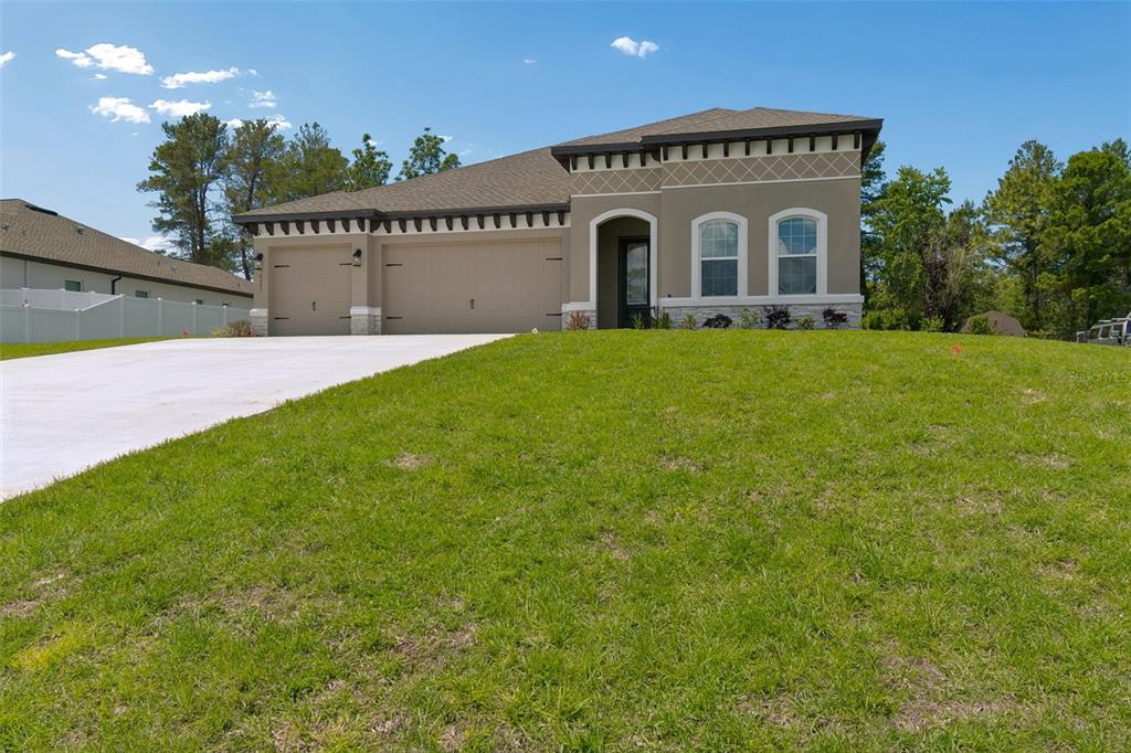 A single-story house with a tan stucco exterior, a three-car garage, and a grassy lawn — 8283 NITTANY ROAD, WEEKI WACHEE, FL