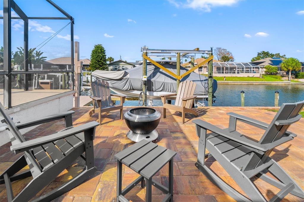 A patio with four Adirondack chairs and a fire pit overlooking a canal and boat — 5 CHEYENNE COURT, PALM COAST, FL