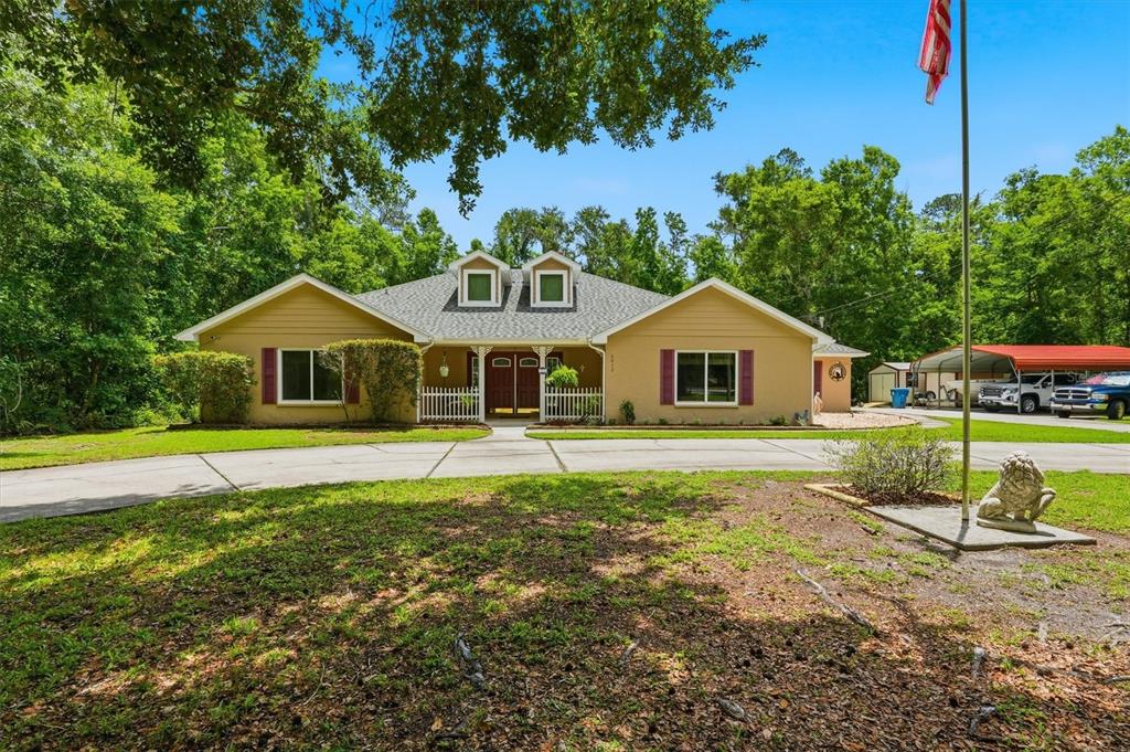 A tan, single-story house with a white picket fence, dormer windows, and a metal carport — 6012 VALLEY SPRING DRIVE, BROOKSVILLE, FL