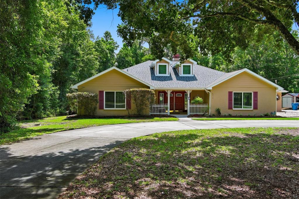 A single-story house with a yellow exterior, red shutters, and a curved concrete driveway — 6012 VALLEY SPRING DRIVE, BROOKSVILLE, FL