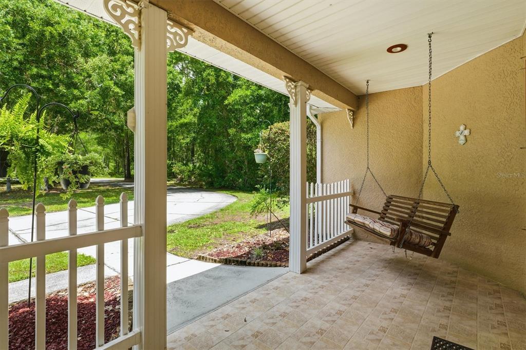 A covered porch features a hanging wooden swing, tiled flooring, and a white picket railing — 6012 VALLEY SPRING DRIVE, BROOKSVILLE, FL