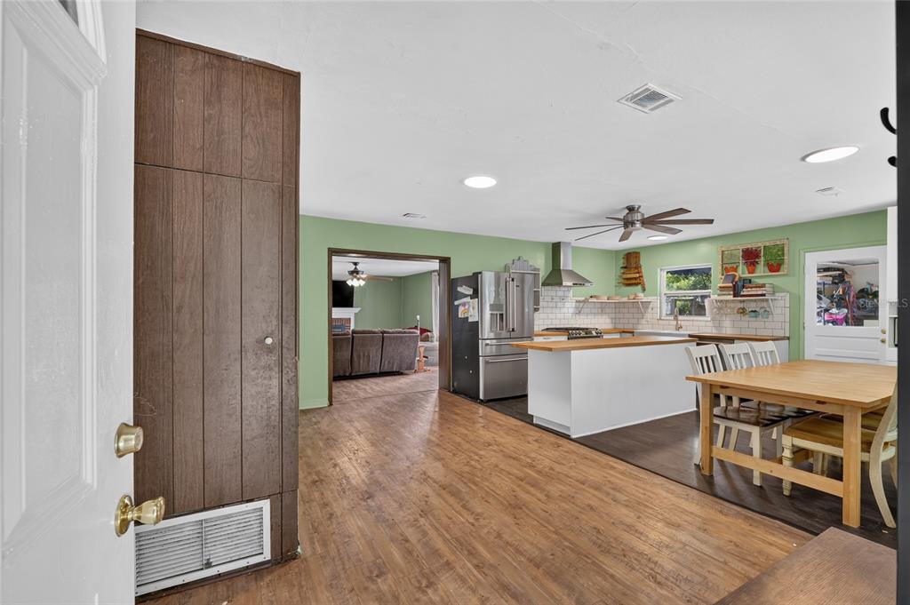 An open-concept kitchen and dining area features wood-look flooring, white cabinets, and green walls — 1805 NE 6TH TERRACE, GAINESVILLE, FL