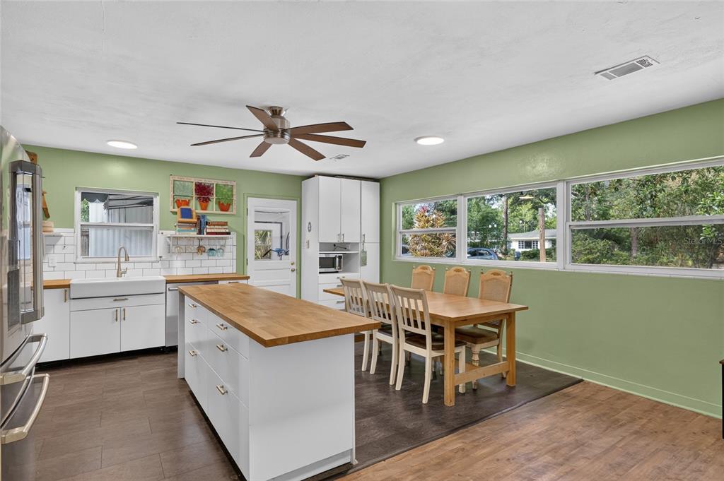 A kitchen with white cabinets, a wood-topped island, green walls, and a dining area — 1805 NE 6TH TERRACE, GAINESVILLE, FL