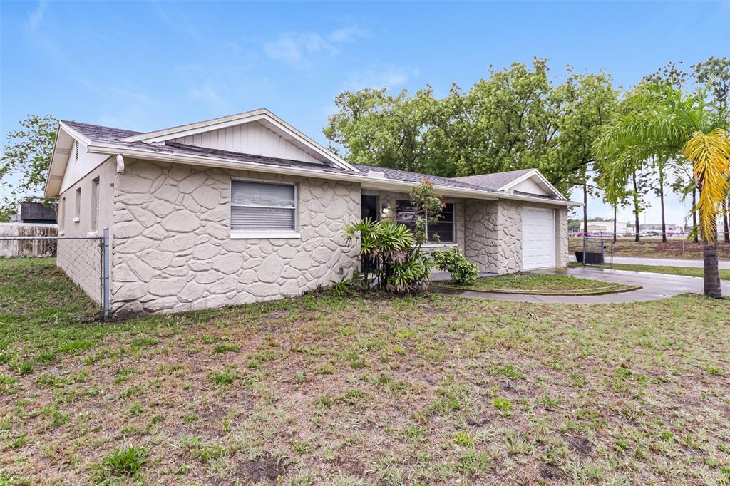 A single-story house with a stone-textured exterior, a front-facing garage, and a chain-link fence — 7004 MAYFIELD DRIVE, PORT RICHEY, FL