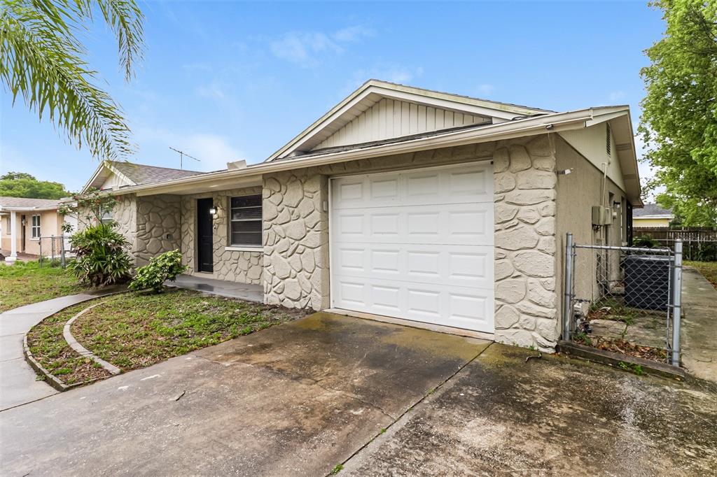 A single-story house with a white garage door, stone facade, and a concrete driveway — 7004 MAYFIELD DRIVE, PORT RICHEY, FL