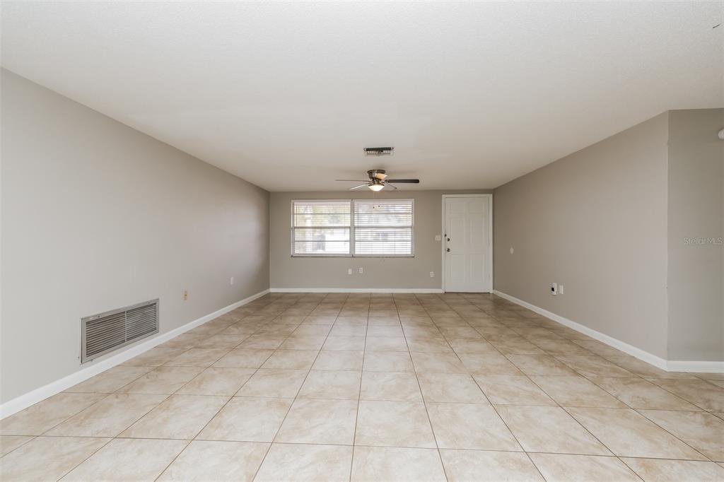 An empty room features light-colored tile flooring, beige walls, a ceiling fan, and a window — 7004 MAYFIELD DRIVE, PORT RICHEY, FL
