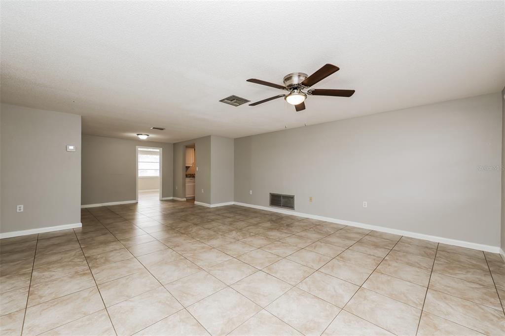 An empty room features light-colored tile flooring, gray walls, and a ceiling fan — 7004 MAYFIELD DRIVE, PORT RICHEY, FL