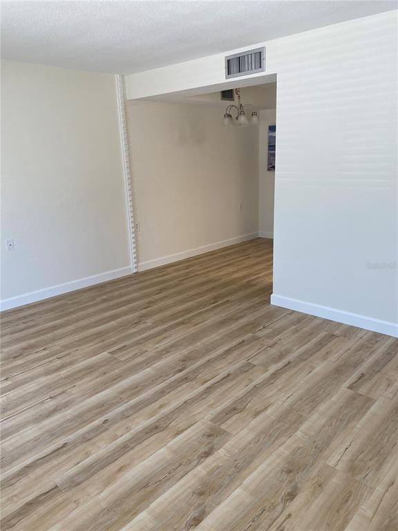 An empty room with light wood-look flooring and a pass-through opening to a dining area — 8325 112TH STREET UNIT 106, SEMINOLE, FL