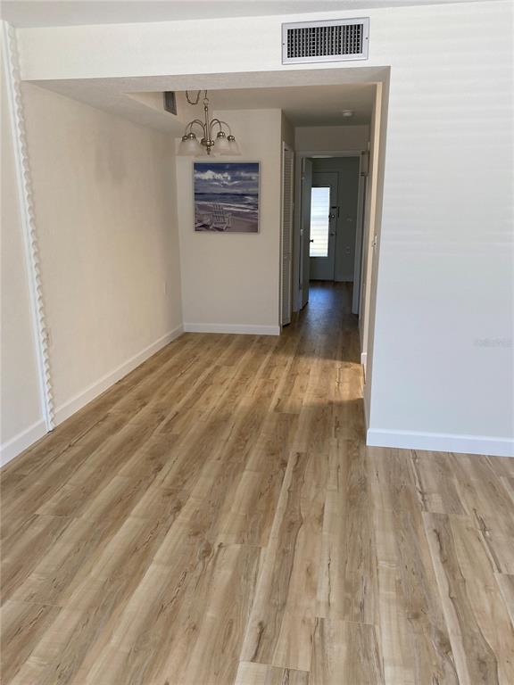 A hallway with light wood-look flooring leads to a doorway with a view of a window — 8325 112TH STREET UNIT 106, SEMINOLE, FL