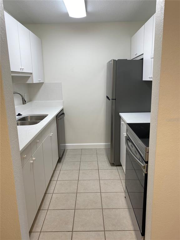 A galley kitchen features white cabinets, stainless steel appliances, white countertops, and light tile flooring — 8325 112TH STREET UNIT 106, SEMINOLE, FL