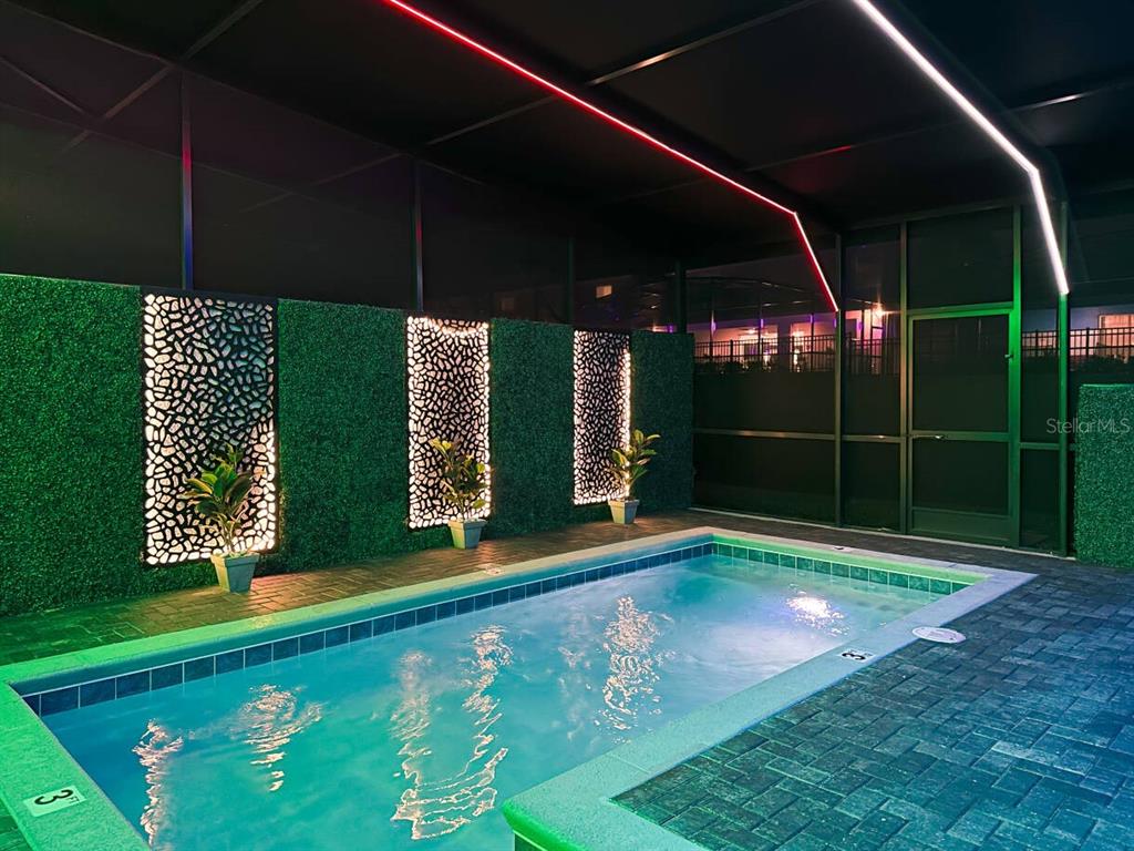 An illuminated rectangular swimming pool sits inside a screened enclosure with decorative wall panels — 996 PARADISE DRIVE, DAVENPORT, FL