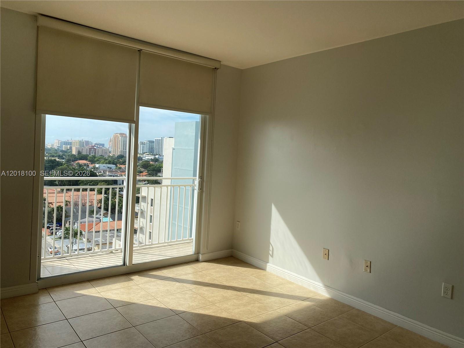 An empty room with beige tile flooring, light-colored walls, and a sliding glass balcony door — 2425 SW 27th Ave # 1008, Miami FL 33145, MIAMI, FL