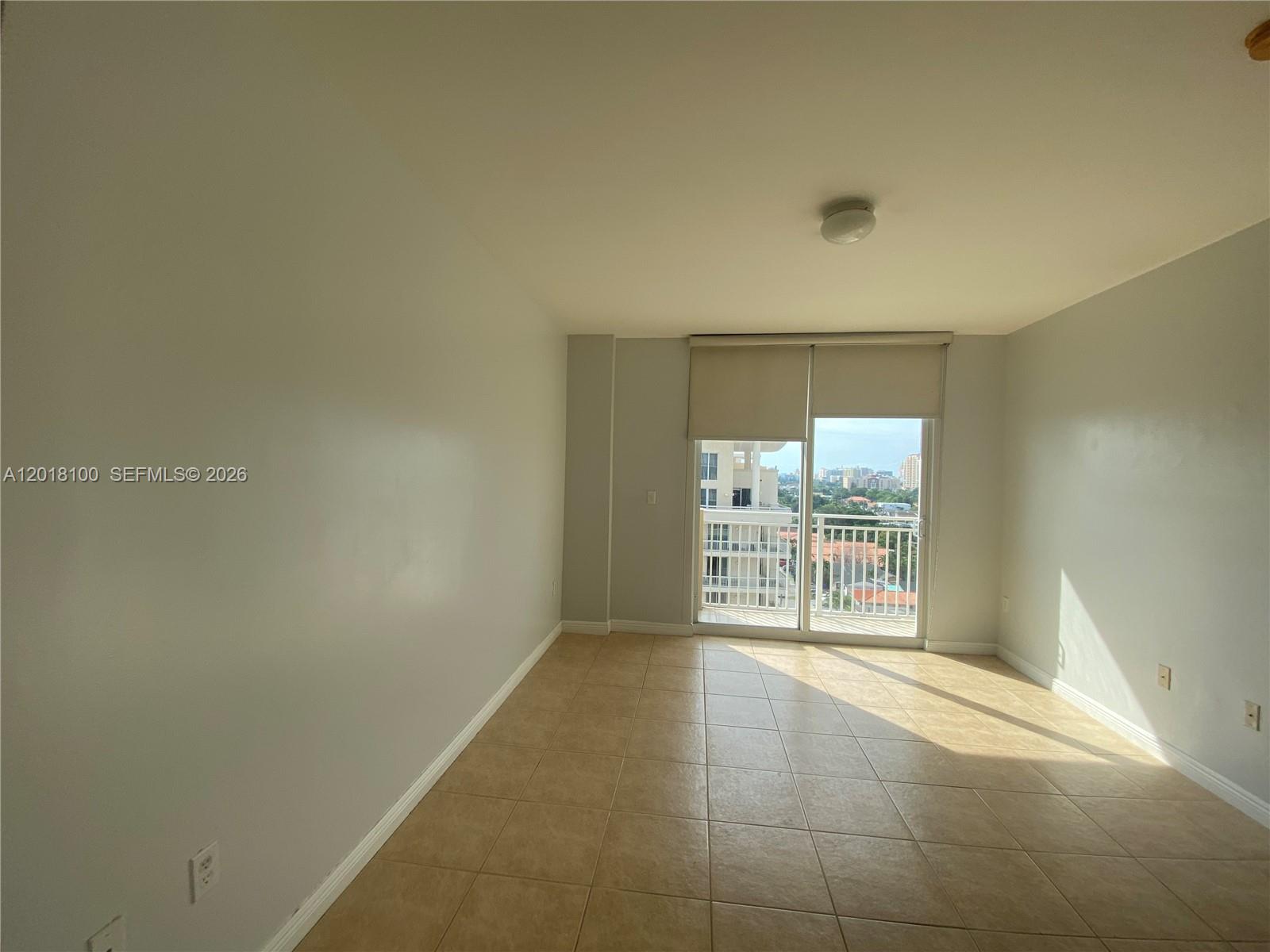 An empty room features light-colored walls, tiled flooring, and a sliding glass door to a balcony — 2425 SW 27th Ave # 1008, Miami FL 33145, MIAMI, FL
