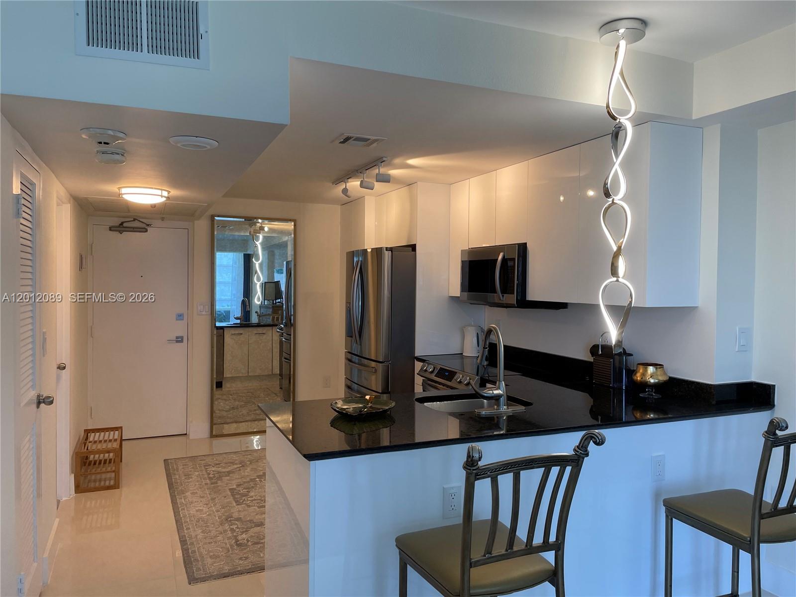 A modern kitchen features white cabinets, black countertops, stainless steel appliances, and a pendant light — 10275 Collins Ave # 602, Bal Harbour FL 33154, BAL HARBOUR, FL