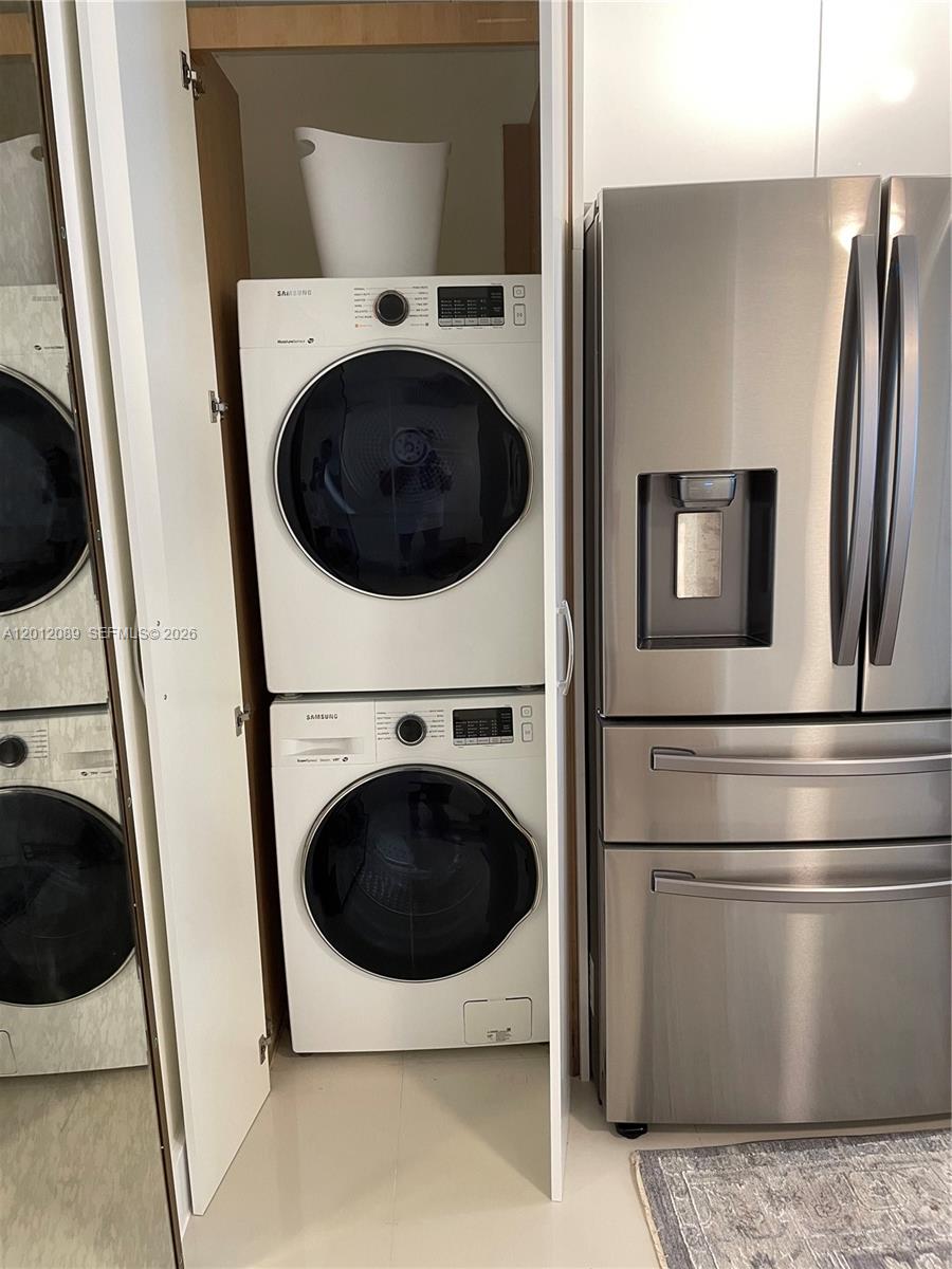 A stacked Samsung washer and dryer unit sit in a closet next to a stainless-steel refrigerator — 10275 Collins Ave # 602, Bal Harbour FL 33154, BAL HARBOUR, FL
