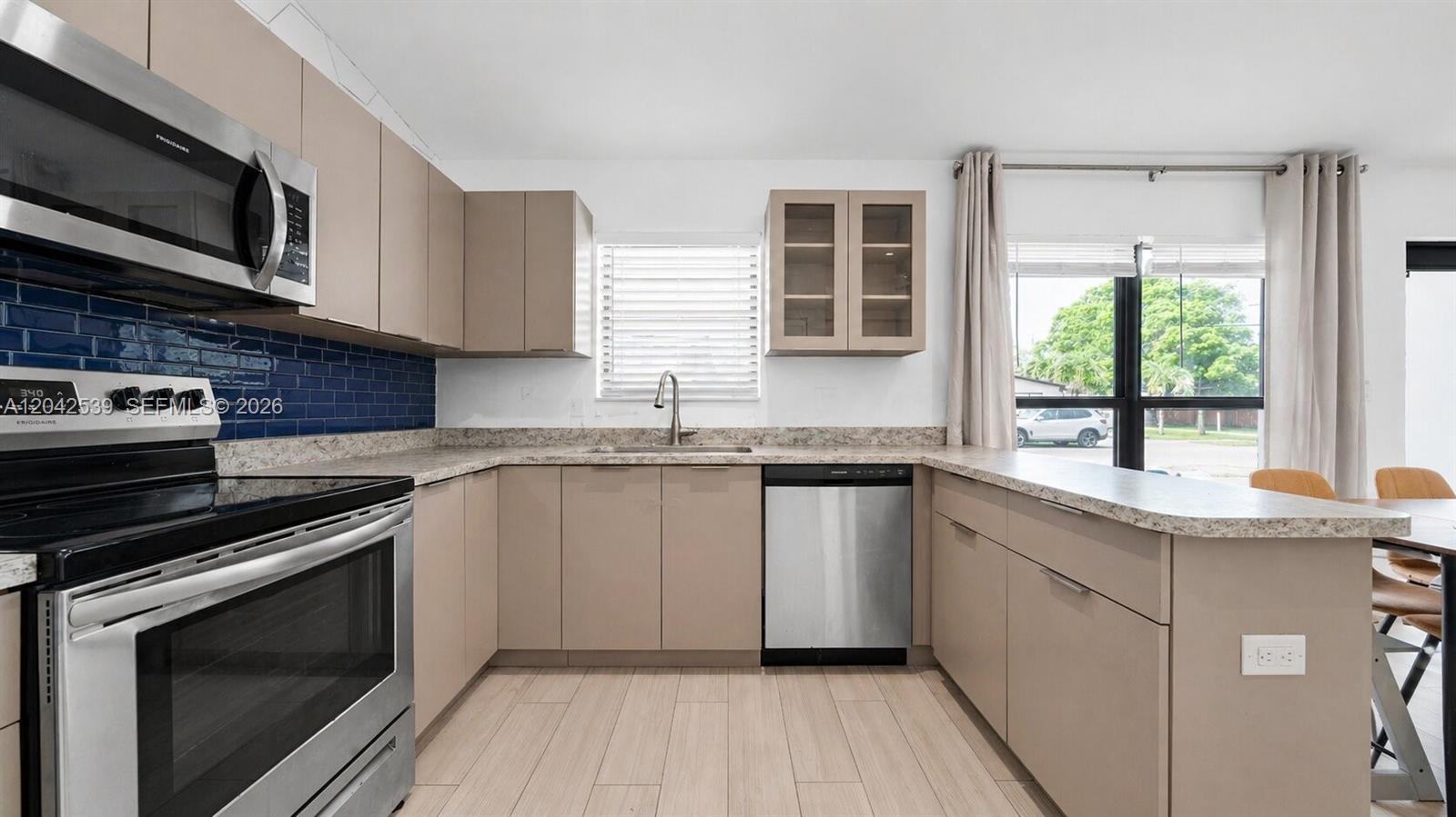 A kitchen features light brown cabinets, stainless steel appliances, a blue tile backsplash, and a window — 1704 Rodman St # 1, Hollywood FL 33020, HOLLYWOOD, FL