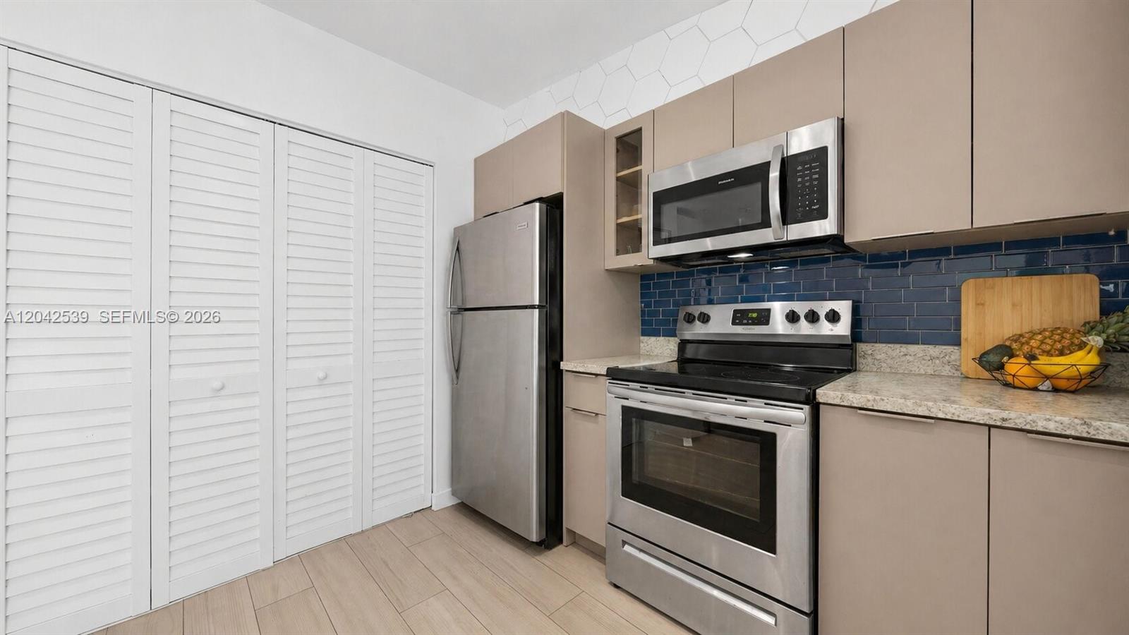 A kitchen features stainless steel appliances, light-toned cabinets, and a blue subway tile backsplash — 1704 Rodman St # 1, Hollywood FL 33020, HOLLYWOOD, FL