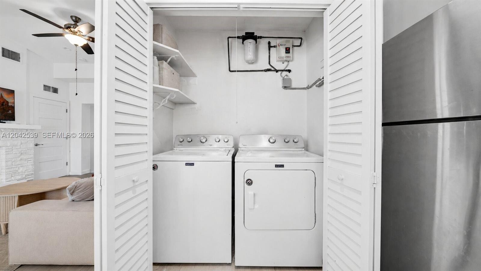 A laundry closet contains a white washer and dryer with shelving and plumbing above — 1704 Rodman St # 1, Hollywood FL 33020, HOLLYWOOD, FL