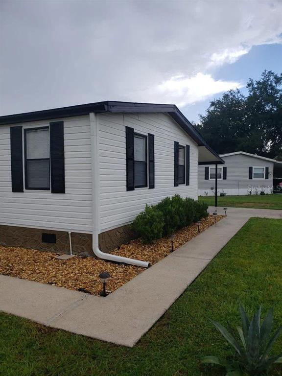 A white mobile home with black shutters and a gravel landscaping bed along the side — 2557 LAKOTA LANE, ST CLOUD, FL