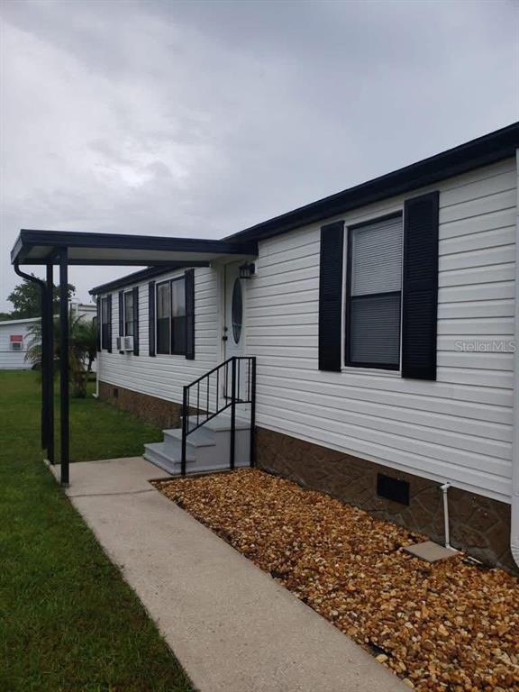 A white mobile home exterior features a covered entryway, black shutters, and a gravel garden bed — 2557 LAKOTA LANE, ST CLOUD, FL