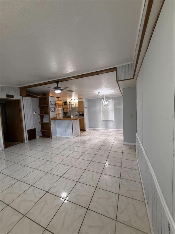 A room with white tile flooring, wood-paneled walls, a ceiling fan, and an open kitchen — 2557 LAKOTA LANE, ST CLOUD, FL