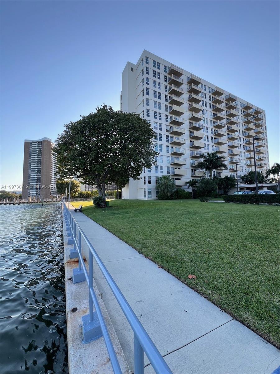 A tall apartment building stands next to a grassy lawn and a waterfront walkway — 880 NE 69th St # 11M, Miami FL 33138, MIAMI, FL