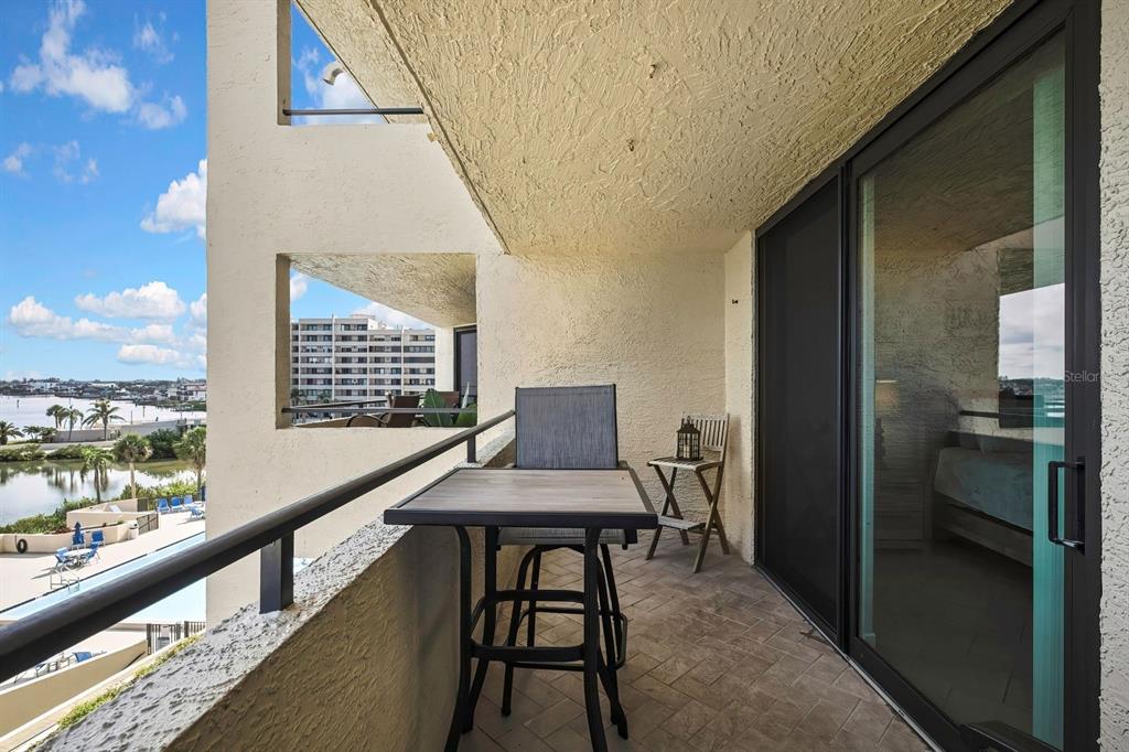 A balcony with a small table and chairs overlooks a swimming pool and water — 6009 SEA RANCH DRIVE UNIT 414, HUDSON, FL