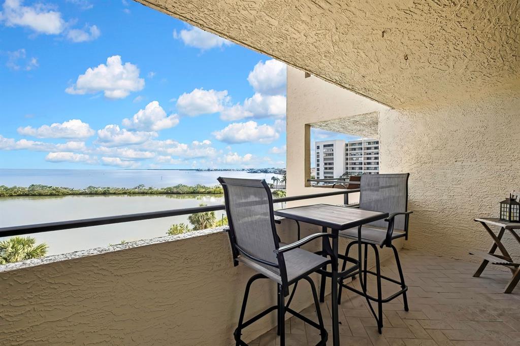 A balcony with a table and two chairs overlooks a body of water and buildings — 6009 SEA RANCH DRIVE UNIT 414, HUDSON, FL