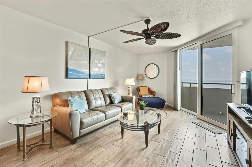 A living room features a leather sofa, glass tables, a ceiling fan, and a balcony view — 6009 SEA RANCH DRIVE UNIT 414, HUDSON, FL
