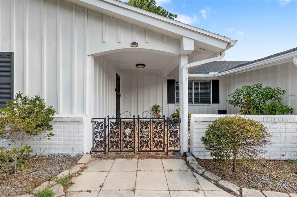 A white house exterior features a covered entryway enclosed by a decorative black metal gate — 8517 SUNFLOWER LANE, HUDSON, FL