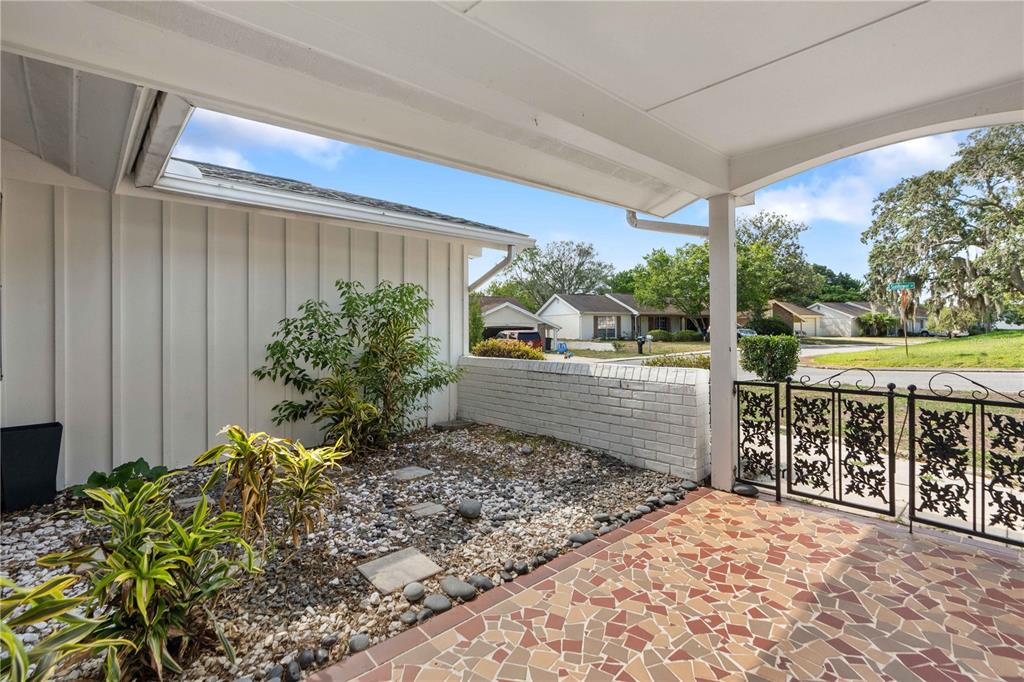 A covered patio features a mosaic tile floor, a rock garden, and a metal gate — 8517 SUNFLOWER LANE, HUDSON, FL
