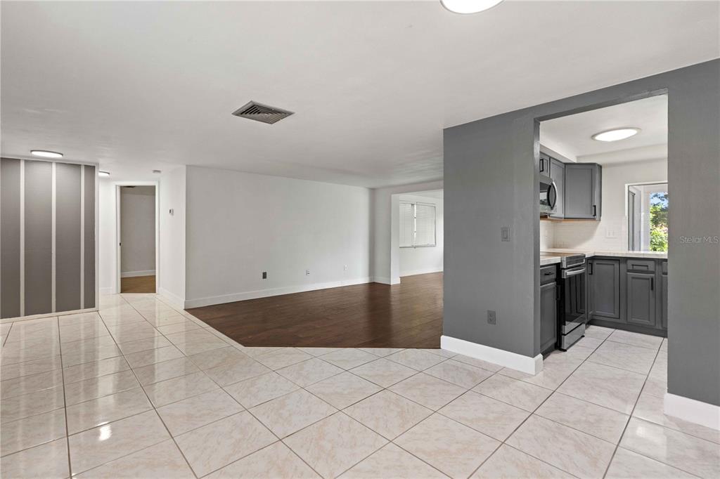 A living area with tile and wood flooring transitions into a kitchen with gray cabinets — 8517 SUNFLOWER LANE, HUDSON, FL