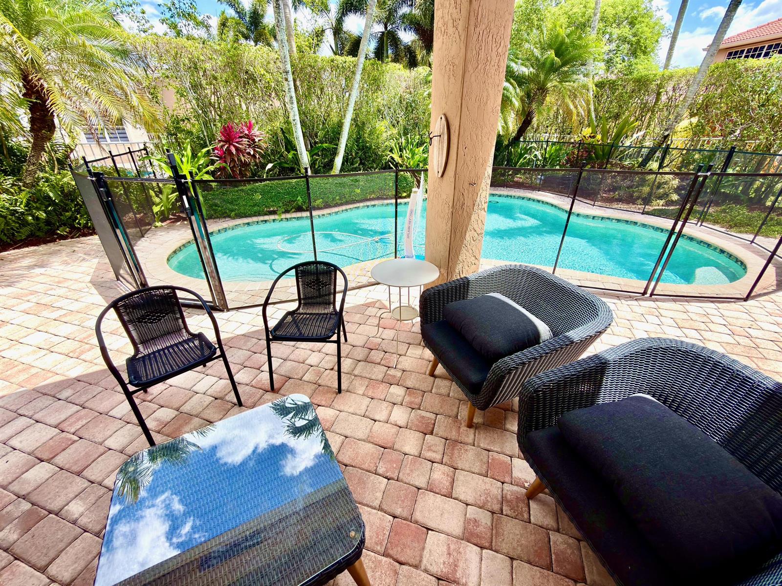 A patio with outdoor seating overlooks a swimming pool enclosed by a black safety fence — 1618 Royal Grove Way, Weston FL 33327, WESTON, FL
