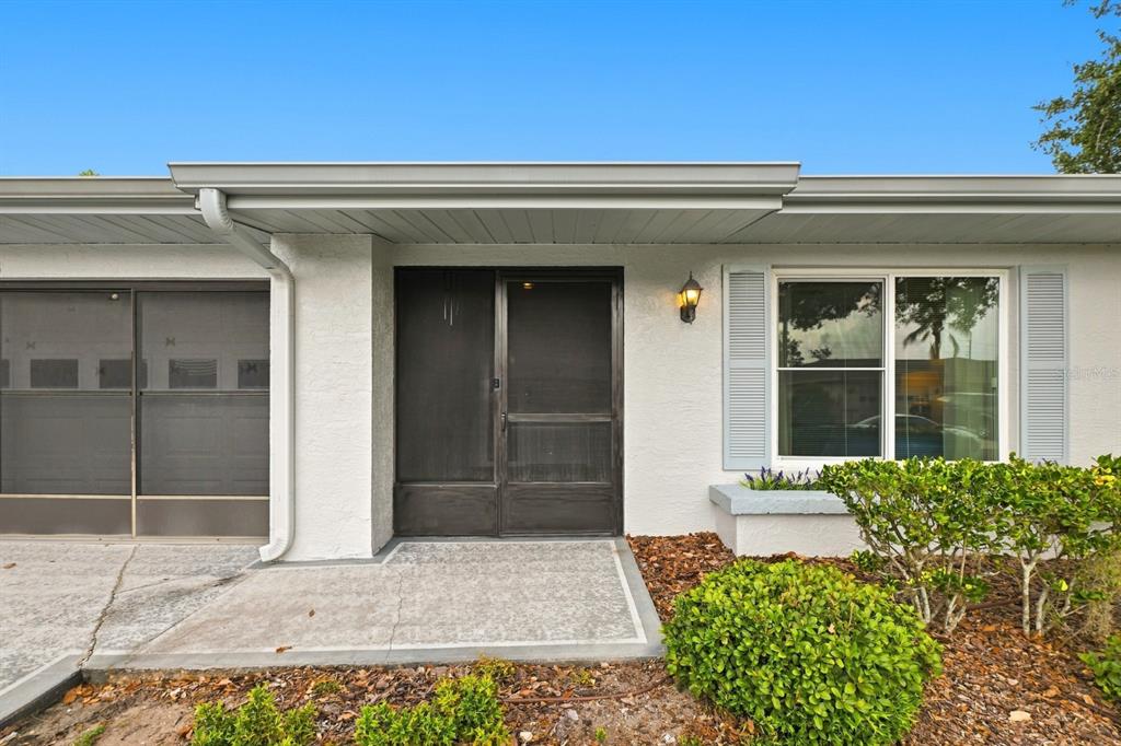 The exterior of a house features a screened front door, a window, and landscaping — 1425 LELAND DRIVE, SUN CITY CENTER, FL