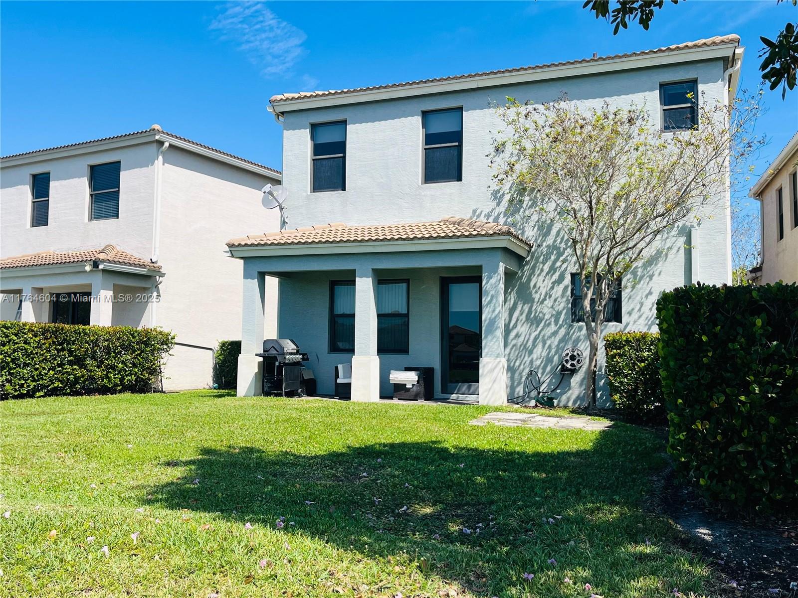 The exterior of a two-story house features a covered patio, a grill, and a lawn — 616 NE 193rd St, Miami FL 33179, MIAMI, FL