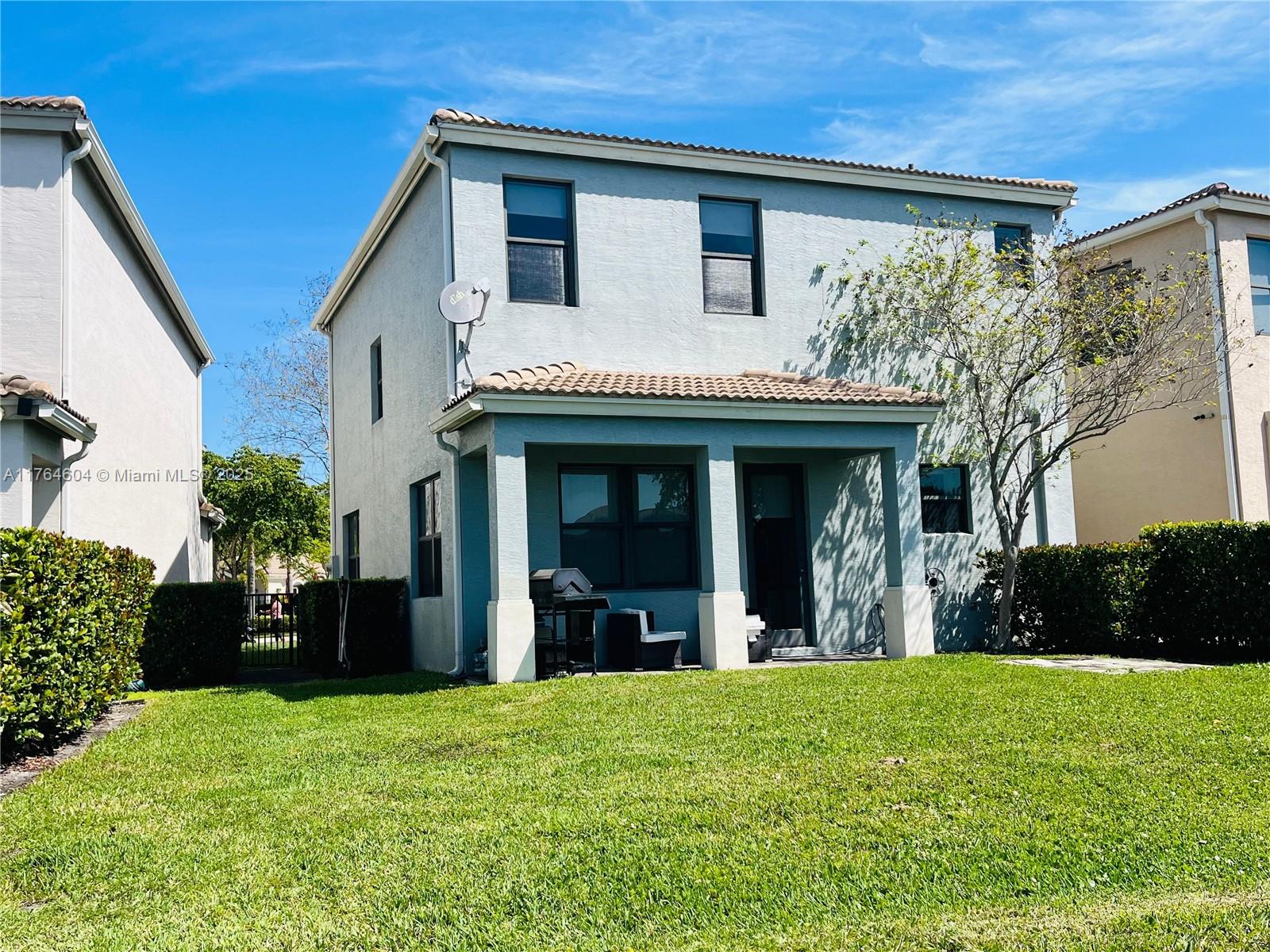 The rear exterior of a two-story light blue house features a covered patio and lawn — 616 NE 193rd St, Miami FL 33179, MIAMI, FL