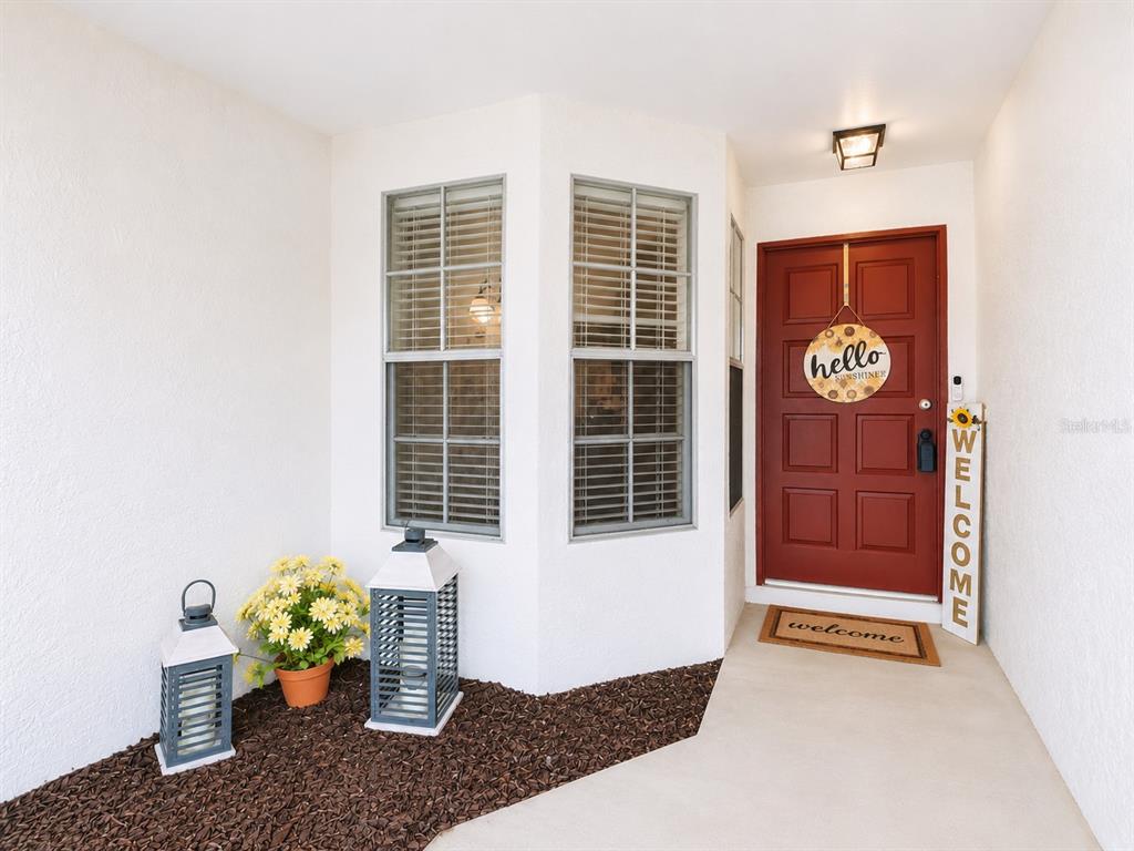 A red front door with a welcome sign sits beside two windows and decorative lanterns — 12008 PEONY COURT, TAMPA, FL