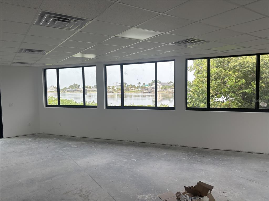 An unfinished room features a drop ceiling, concrete floors, and windows overlooking a waterfront view — 1499 S MCCALL ROAD, ENGLEWOOD, FL