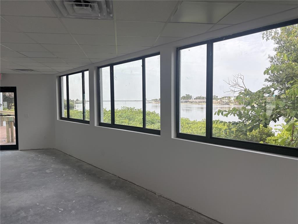 An unfinished room features white walls, a concrete floor, and large windows overlooking a bay — 1499 S MCCALL ROAD, ENGLEWOOD, FL