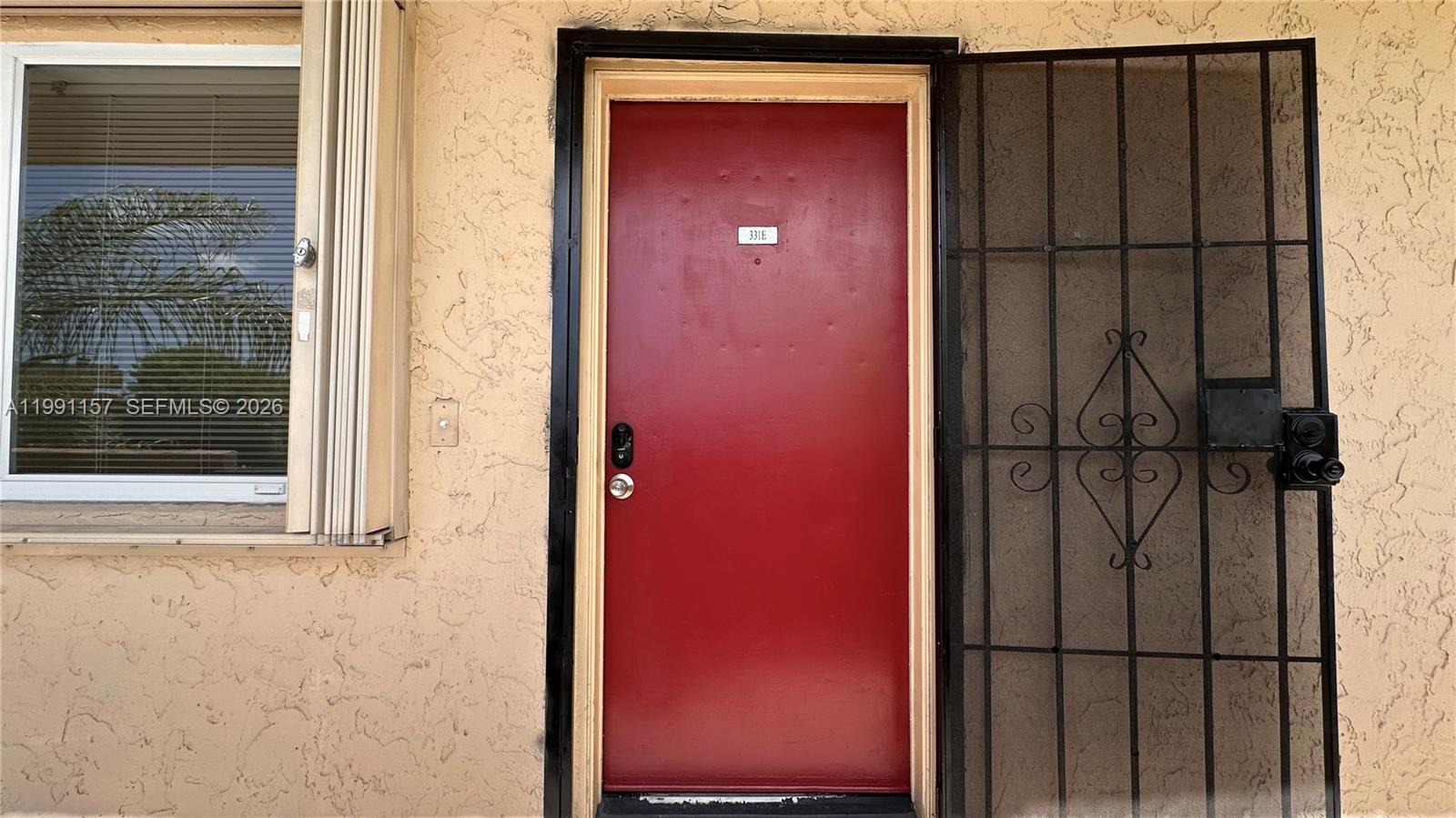 A red front door with a security gate is set in a textured beige wall — 8401 SW 107th Ave # 331E, Miami FL 33173, MIAMI, FL