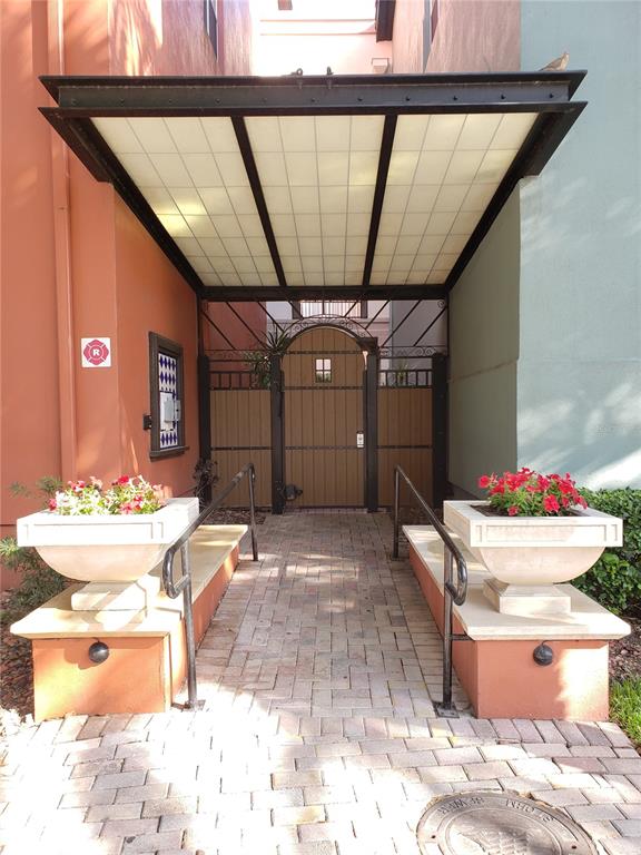 A paved walkway leads to a gated entrance under a metal-framed canopy with two planters — 402 S ARMENIA AVENUE UNIT 114, TAMPA, FL