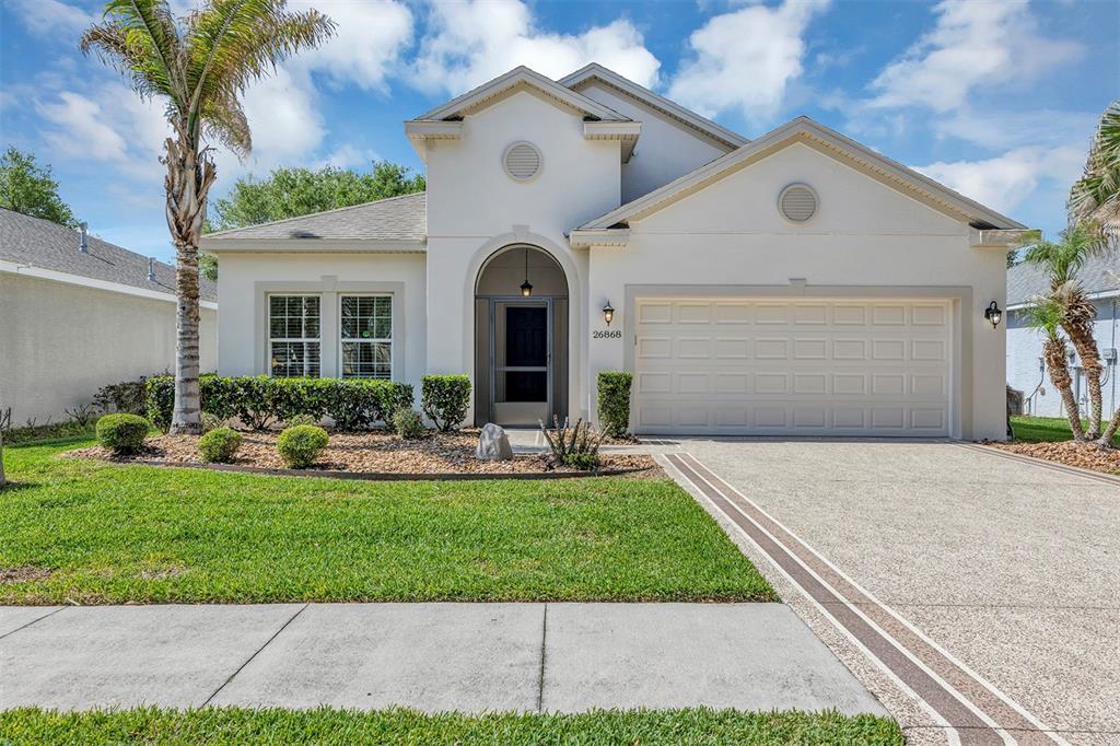A single-story suburban house with a white stucco facade, arched entryway, and a two-car garage — 26868 WHITE PLAINS WAY, LEESBURG, FL
