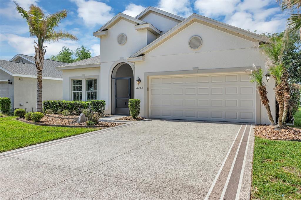 A single-story house with a white stucco exterior, a two-car garage, and a paved driveway — 26868 WHITE PLAINS WAY, LEESBURG, FL