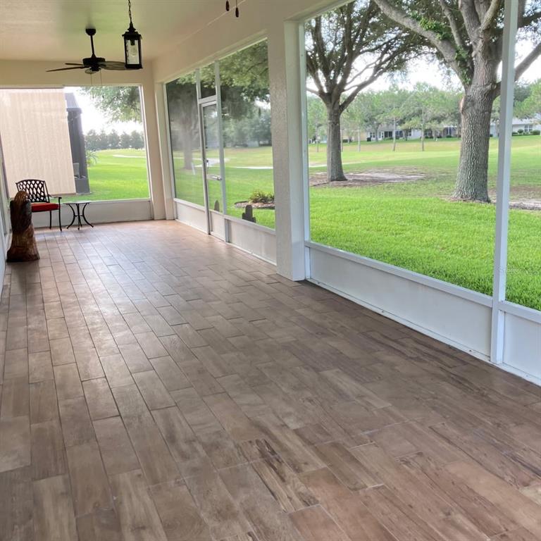 A screened-in porch with wood-look tile flooring overlooks a grassy yard and trees — 26868 WHITE PLAINS WAY, LEESBURG, FL